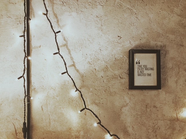 A framed quote hanging on the wall next to string lights. The quote reads: Time you enjoy wasting is not wasted time.